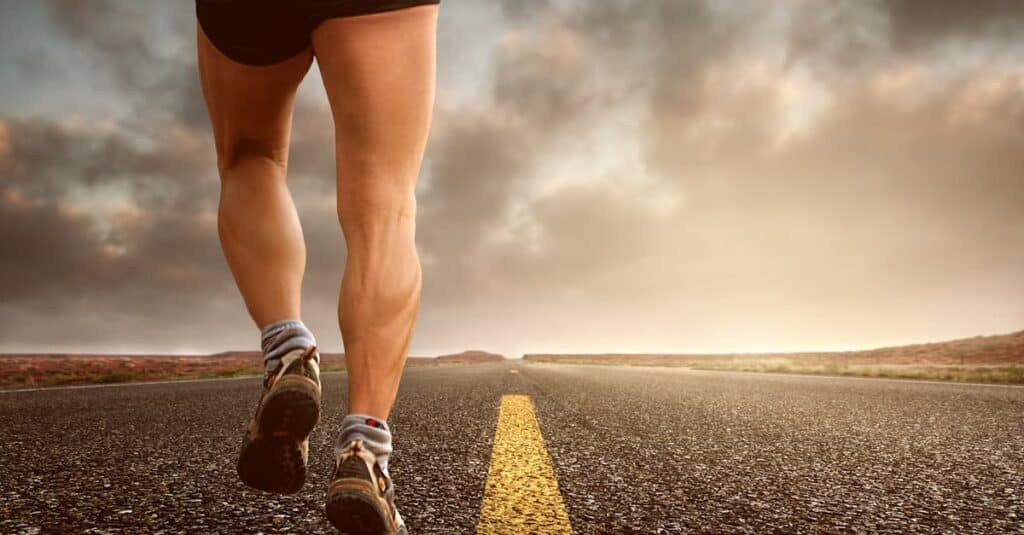 Runner's legs on a road during a sunset, symbolizing endurance and outdoor fitness training.