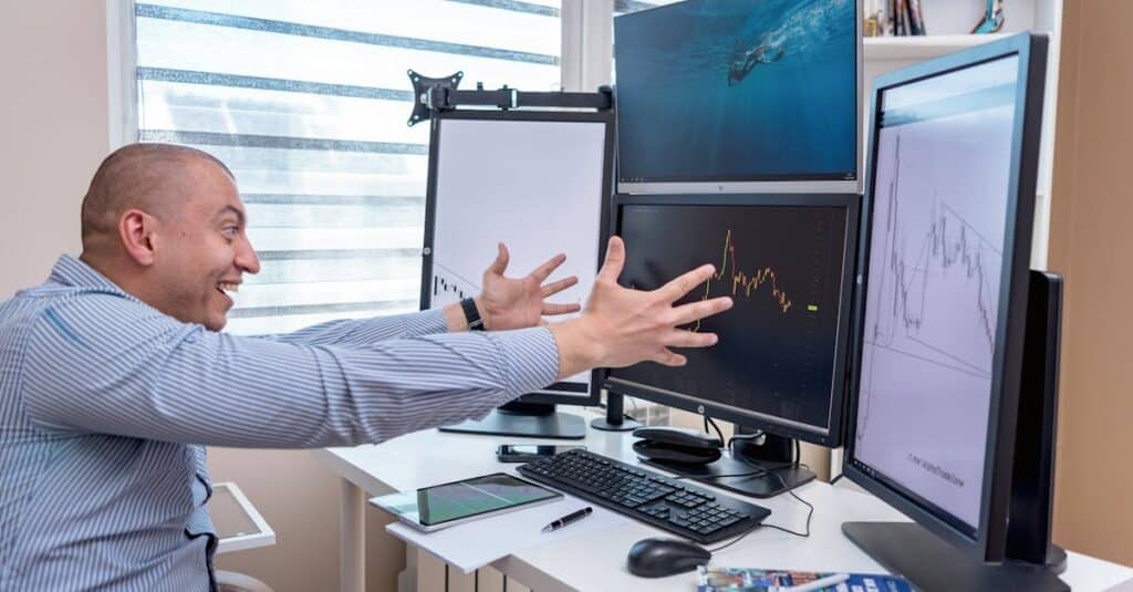 A joyful day trader celebrates a market victory in a modern office setup with multiple monitors displaying stock charts.