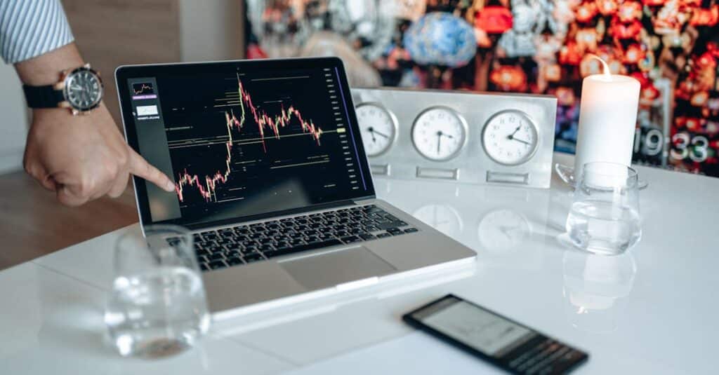 Businessman pointing at a financial graph on a laptop screen, showcasing stock market analysis.