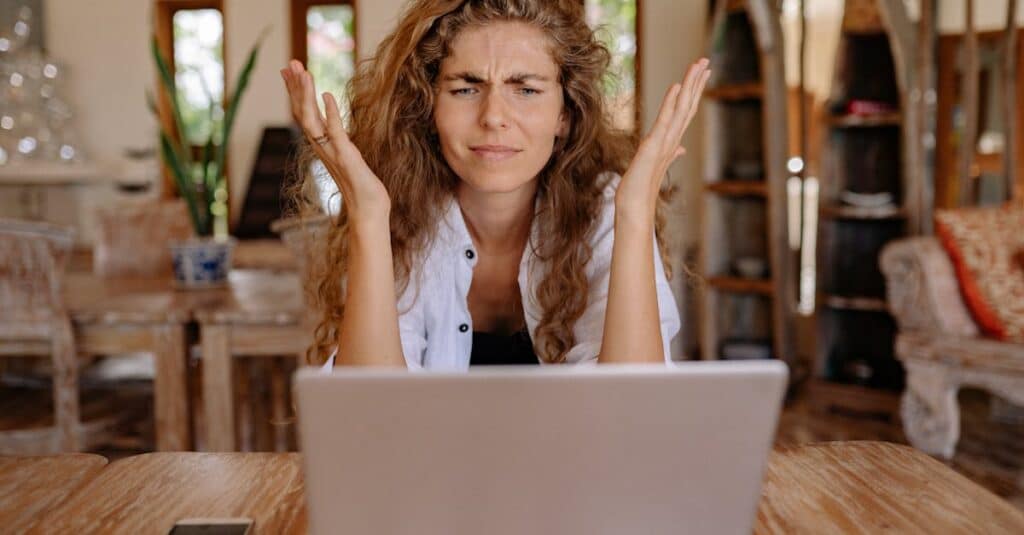 A woman frustrated with her laptop while working remotely indoors, expressing stress.