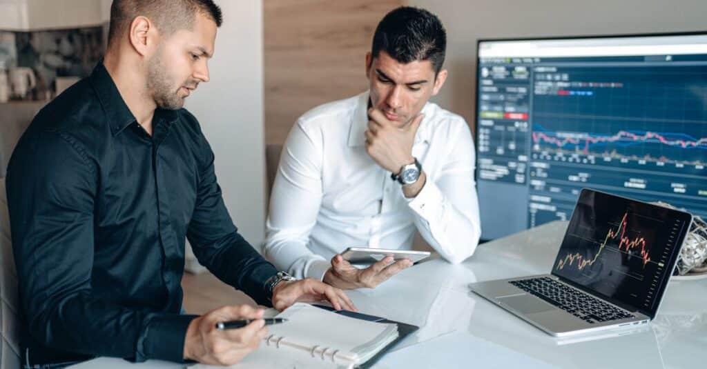 Two businessmen discussing stock market analytics in a modern office setting.